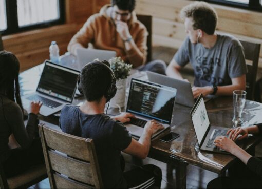 a group of people sitting around a table with laptops